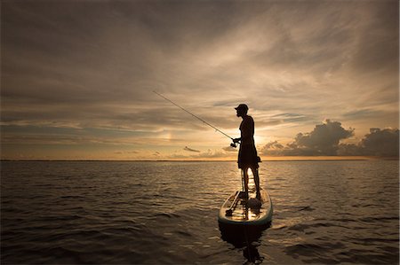 sportfishing - Man standing on paddle board, on water, at sunset, holding fishing rod Stock Photo - Premium Royalty-Free, Code: 614-09038629