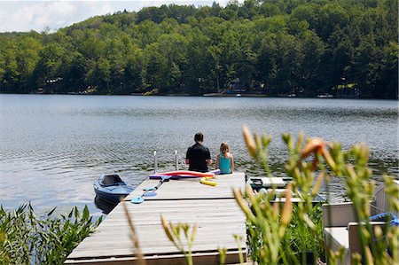 simsearch:614-09038795,k - Two girls sitting on jetty beside lake, rear view Fotografie stock - Premium Royalty-Free, Codice: 614-09038780