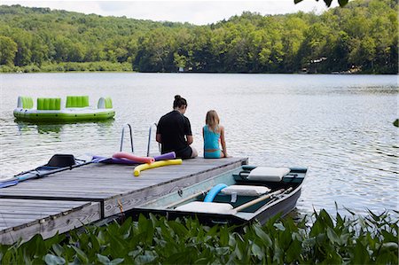 simsearch:614-09038795,k - Two girls sitting on jetty beside lake, rear view Fotografie stock - Premium Royalty-Free, Codice: 614-09038781