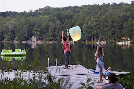 simsearch:614-09038795,k - Girl standing on jetty releasing sky lantern, young girl watching, woman photographing event using smartphone Fotografie stock - Premium Royalty-Free, Codice: 614-09038792