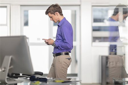 simsearch:649-08577542,k - Young male office worker looking at smartphone in office Stock Photo - Premium Royalty-Free, Code: 614-09038829