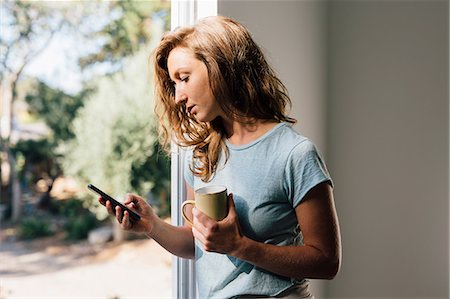 problem - Young woman at patio door looking at smartphone Stock Photo - Premium Royalty-Free, Code: 614-09056596
