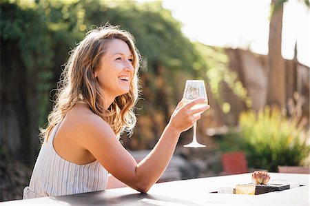 Young woman sitting outdoors, holding wine glass, smiling Foto de stock - Royalty Free Premium, Número: 614-09056602