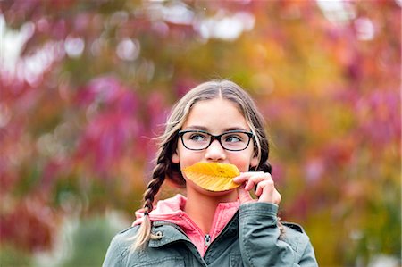 simsearch:614-09056681,k - Portrait of girl with plaits and glasses covering mouth with leaf looking away Fotografie stock - Premium Royalty-Free, Codice: 614-09056681