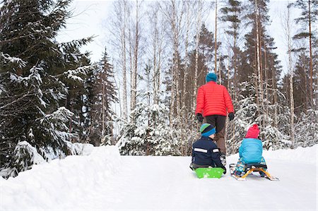 Rear view of man pulling two sons on toboggans through snow covered forest Stock Photo - Premium Royalty-Free, Code: 614-09056730
