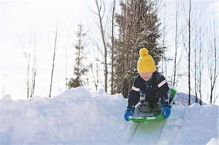 simsearch:614-09212275,k - Boy in yellow knit hat tobogganing on snow covered hill Photographie de stock - Premium Libres de Droits, Code: 614-09056741