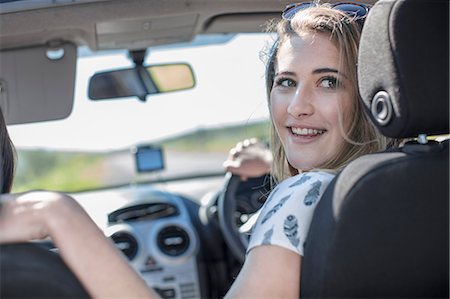 Young woman driving car, looking over shoulder, smiling Stock Photo - Premium Royalty-Free, Code: 614-09056828