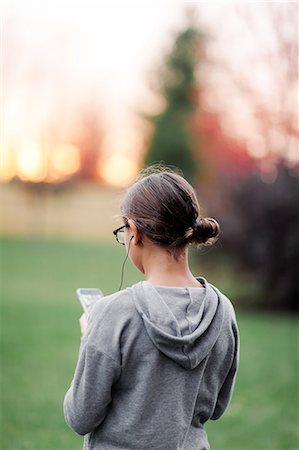 Rear view of girl listening to earphone music looking at smartphone in garden Stock Photo - Premium Royalty-Free, Code: 614-09079156