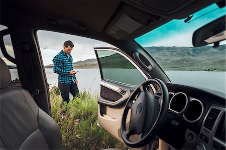 Mid adult man standing beside Dillon Reservoir, holding smartphone, view through parked car, Silverthorne, Colorado, USA Foto de stock - Sin royalties Premium, Código: 614-09127238