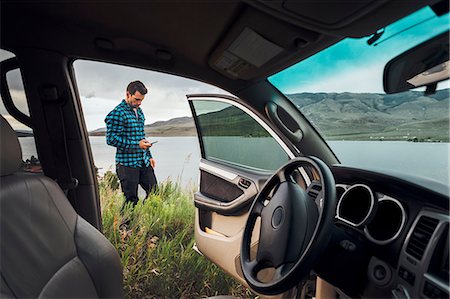 signal - Mid adult man standing beside Dillon Reservoir, holding smartphone, view through parked car, Silverthorne, Colorado, USA Stock Photo - Premium Royalty-Free, Code: 614-09127238