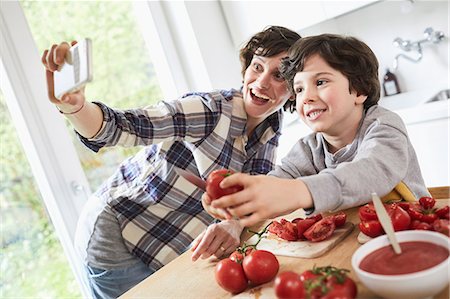 simsearch:614-08383716,k - Mother and son preparing food in kitchen, mother taking selfie using smartphone Foto de stock - Sin royalties Premium, Código: 614-09127328