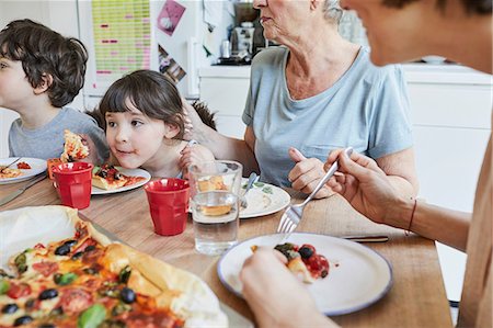 Three generation family sitting at kitchen table eating pizza Stock Photo - Premium Royalty-Free, Code: 614-09127366