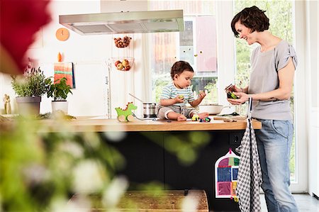 Baby daughter sitting on kitchen counter watching mother prepare vegetables Stock Photo - Premium Royalty-Free, Code: 614-09127376