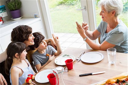 simsearch:640-08089329,k - Grandmother sitting at kitchen, photographing grown daughter and grandchildren, using smartphone Stock Photo - Premium Royalty-Free, Code: 614-09127415