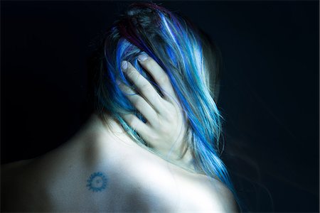 Rear view of woman with hand in her blue hair, low key studio shot Stock Photo - Premium Royalty-Free, Code: 614-09134997