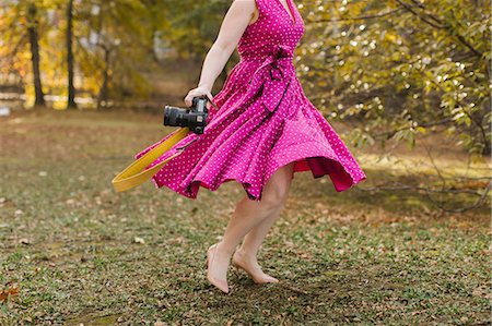 pink - Young woman with camera dancing in park, neck down Stock Photo - Premium Royalty-Free, Code: 614-09147732
