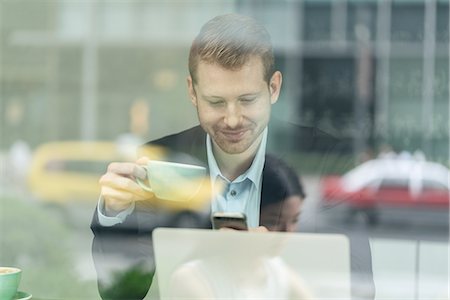 simsearch:649-09078403,k - Businessman sitting in cafe, drinking coffee, using smartphone, viewed through window Stock Photo - Premium Royalty-Free, Code: 614-09156728