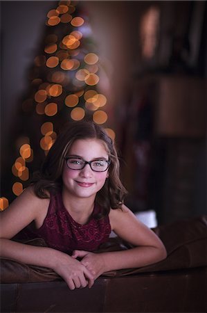 rosy cheeks - Girl leaning over sofa, smiling, Christmas tree in background Stock Photo - Premium Royalty-Free, Code: 614-09159644