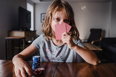 Girl hiding behind playing cards with gambling chips at table, portrait Stock Photo - Premium Royalty-Free, Code: 614-09183031