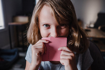 Girl hiding behind playing cards in living room, portrait Stock Photo - Premium Royalty-Free, Code: 614-09183033