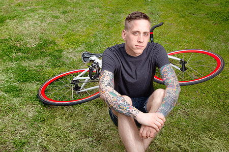 photos of tattooed people on bicycles - Portrait of young tattooed man sitting on grass Stock Photo - Premium Royalty-Free, Code: 614-09210168