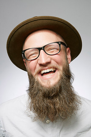 Studio portrait of laughing mid adult man in trilby with overgrown beard Stock Photo - Premium Royalty-Free, Code: 614-09211506