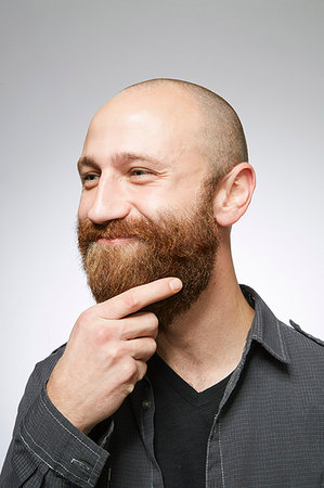 simsearch:614-06974752,k - Studio portrait of mid adult man with shaved hair stroking overgrown beard Photographie de stock - Premium Libres de Droits, Code: 614-09211509