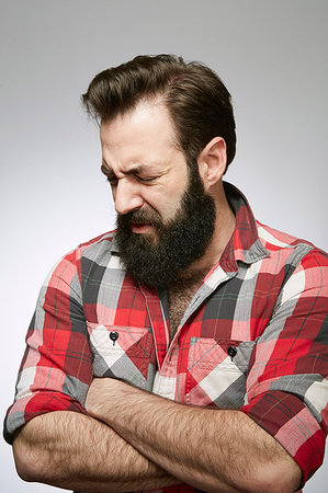 Studio portrait of anguished bearded young man with arms folded Stock Photo - Premium Royalty-Free, Code: 614-09211514