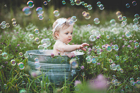 Baby girl in tin bathtub in meadow reaching for floating bubbles Stock Photo - Premium Royalty-Free, Code: 614-09211634