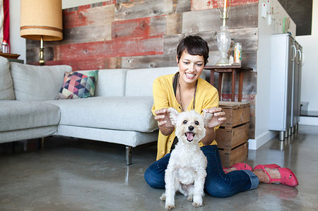 Young woman holding up dogs ears in living room Stock Photo - Premium Royalty-Free, Code: 614-09211709