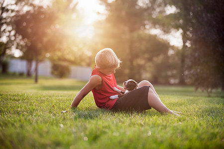 simsearch:614-03020295,k - Side view of boy sitting on grass, Boston Terrier puppy on lap, looking down Fotografie stock - Premium Royalty-Free, Codice: 614-09212160