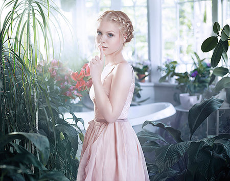 Young woman with finger to lips, standing in bathroom filled with plants Stock Photo - Premium Royalty-Free, Code: 614-09212403