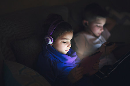 Boy and girl side by side on sofa wearing earphones using digital tablets Stock Photo - Premium Royalty-Free, Code: 614-09212425