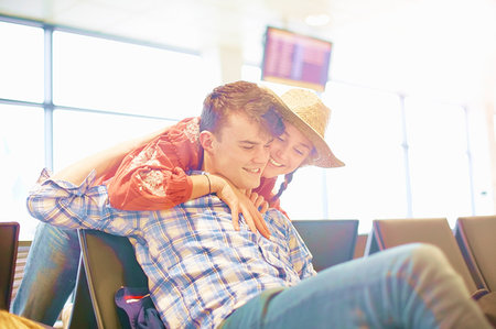 people hugging at airport - Young man sitting at airport, young woman reaching over seat to hug him Stock Photo - Premium Royalty-Free, Code: 614-09213727