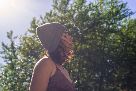 simsearch:614-09213863,k - Young woman in knitted hat contemplating in front of tree foliage, backlit head and shoulder profile Fotografie stock - Premium Royalty-Free, Codice: 614-09213842