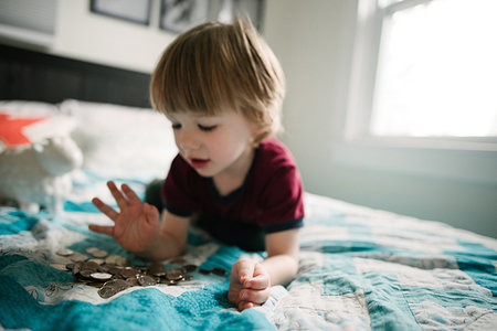 Boy counting coins on bed Stock Photo - Premium Royalty-Free, Code: 614-09245114