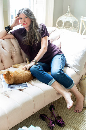 Stylish mature woman sitting on sofa petting ginger cat, portrait Stock Photo - Premium Royalty-Free, Code: 614-09245267