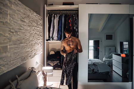 simsearch:614-09258522,k - Mid adult man with tattooed chest getting shirt from wardrobe Stockbilder - Premium RF Lizenzfrei, Bildnummer: 614-09258476