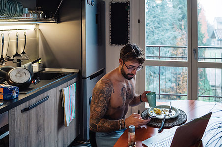 simsearch:614-09258506,k - Mid adult man with tattoos drinking coffee while looking at smartphone Photographie de stock - Premium Libres de Droits, Code: 614-09258498