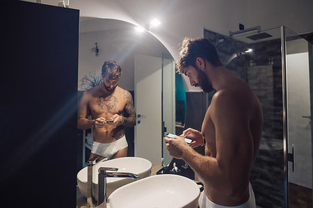 simsearch:649-09078395,k - Mid adult man with tattoos using smartphone touchscreen at bathroom mirror, mirror image Fotografie stock - Premium Royalty-Free, Codice: 614-09258520