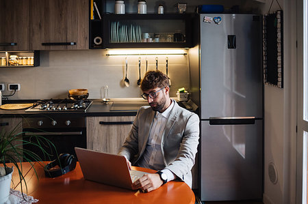 simsearch:614-09258533,k - Mid adult man sitting at kitchen table typing on laptop Stock Photo - Premium Royalty-Free, Code: 614-09258538