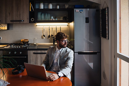 simsearch:614-09258544,k - Mid adult man sitting at kitchen table with laptop looking out through window Photographie de stock - Premium Libres de Droits, Code: 614-09258539