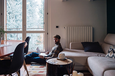 simsearch:614-09258533,k - Mid adult man sitting on living room floor using laptop, portrait Stock Photo - Premium Royalty-Free, Code: 614-09258554