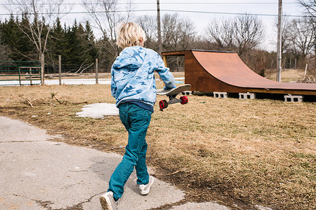 Blond boy carrying skateboard toward rural skateboard ramp, rear view Stock Photo - Premium Royalty-Free, Code: 614-09258753