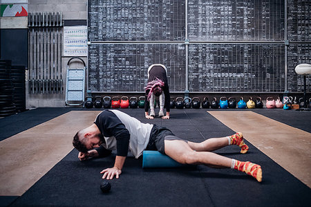 Young man massaging thigh with foam roller in gym Stock Photo - Premium Royalty-Free, Code: 614-09259032