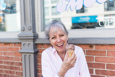 Senior woman sitting on sidewalk with chocolate ice cream cone, portrait Stock Photo - Premium Royalty-Free, Code: 614-09253815