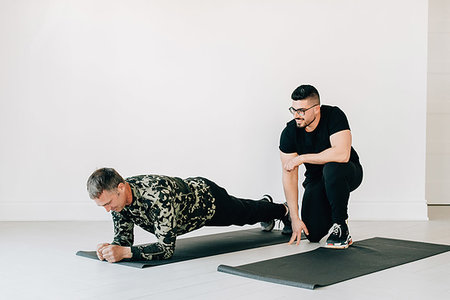 simsearch:614-09276308,k - Fitness instructor observing man doing plank in studio Fotografie stock - Premium Royalty-Free, Codice: 614-09276256