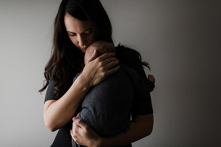 Young woman cradling baby son in arms, low key Stock Photo - Premium Royalty-Free, Code: 614-09276706