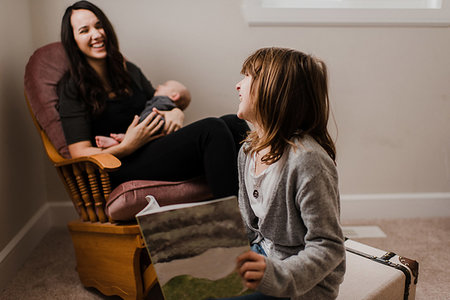 sister sit in brother laps photos - Girl laughing with mother while she cradles baby brother in living room armchair Stock Photo - Premium Royalty-Free, Code: 614-09276700