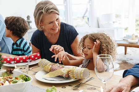 Woman talking to granddaughter playing with Christmas cracker at dining table Stock Photo - Premium Royalty-Free, Code: 614-09276932